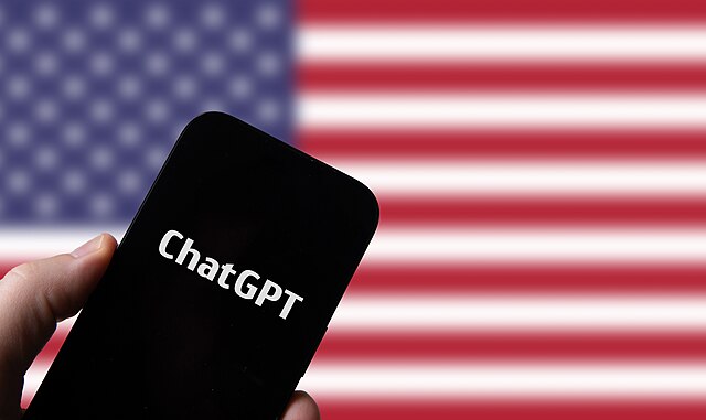 Hand_holding_smartphone_with_OpenAI_Chat_GPT_against_flag_of_USA_(52916339922)