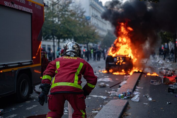 Brannvesen nær en bil som brenner under opptøyer i Paris.