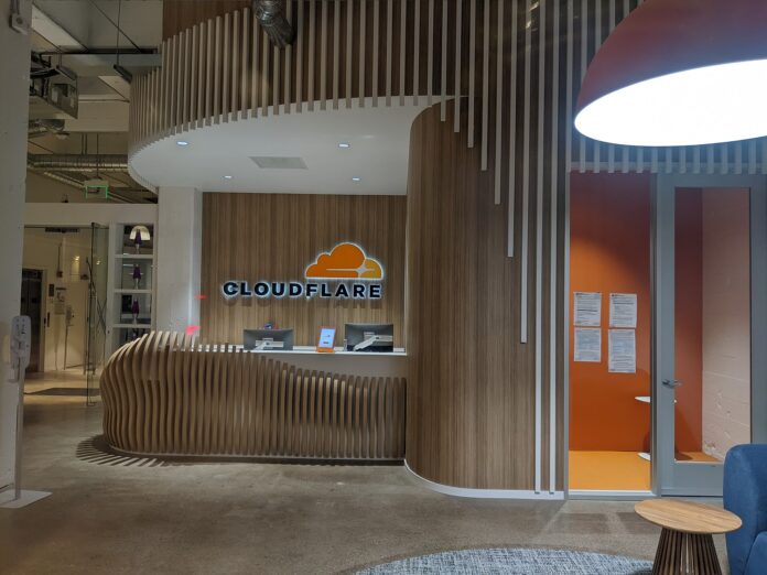 Inngangsparti og resepsjon i Cloudflares kontorer i San Francisco med opplyst Cloudflare-logo på veggen.