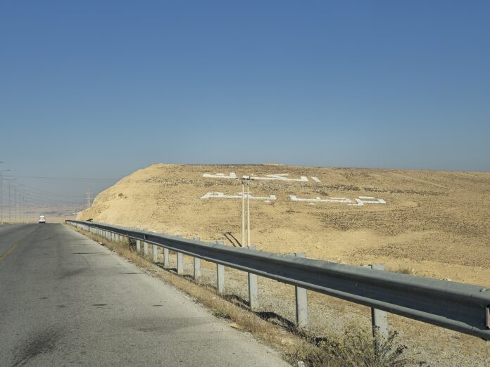 Vei ved innkjøringen til Karak-guvernementet i Jordan, med ørkenlandskap og hvit skrift på en åsside.