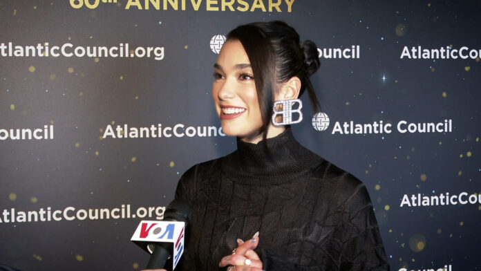 Dua Lipa intervjues foran en vegg med Atlantic Council-logoer.