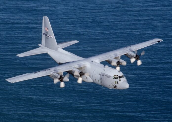 Et grått amerikansk C-130 Hercules militært transportfly i luften over havet.