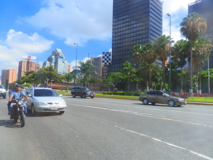 Gatebilde i Caracas med trafikk og CNE-bygningen synlig i bakgrunnen.