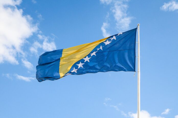 Bosnia-Hercegovinas flagg vaier på en flaggstang mot blå himmel i Sarajevo.