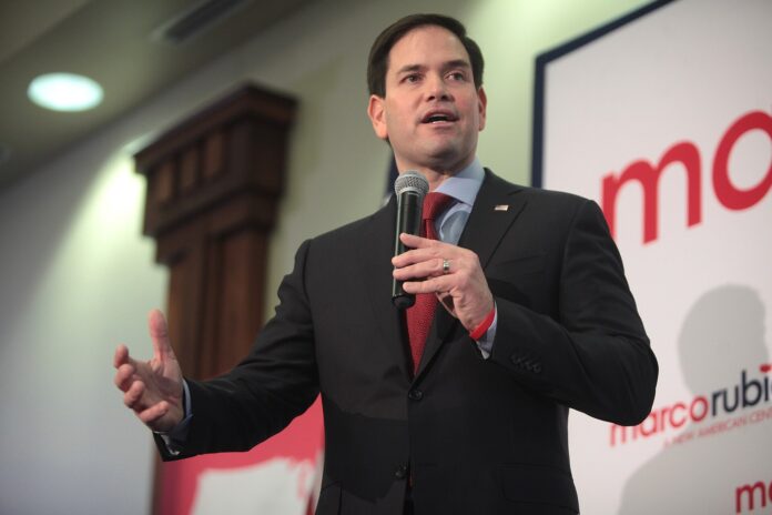 Marco Rubio holder en håndmikrofon og taler fra en scene foran et kampanjeskilt.