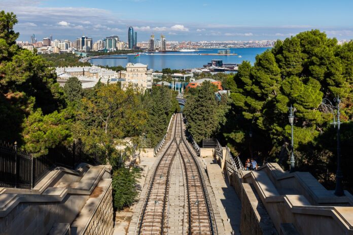 Byutsikt over Baku med bukt, høyhus, trær og skinnegang ned mot vannet.